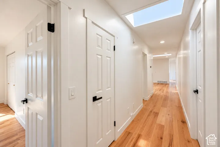 Hallway featuring wood-finish flooring, two skylights, recessed lighting, and doors with matte black hardware