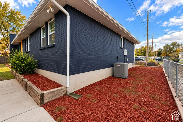 Dark navy brick exterior featuring white trim, concrete foundation, timber-framed planting beds, and external HVAC unit