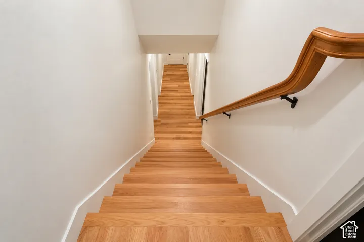Staircase featuring wood-finish treads and landing, complemented by a contoured wood handrail with matte black metal brackets