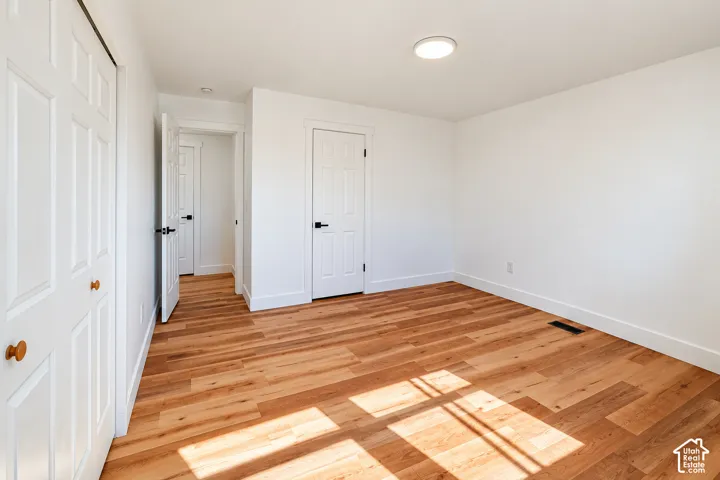 Interior room featuring wood-finish flooring, six-panel interior doors with matte black hardware, and double-door closet cabinetry