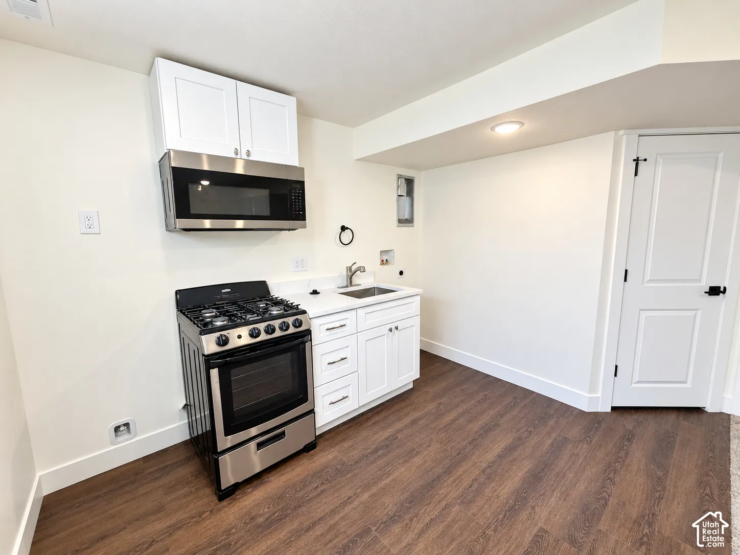 Stainless steel gas range and built-in microwave, white shaker-style cabinetry, drop-in sink with metal faucet, and wood-finish flooring