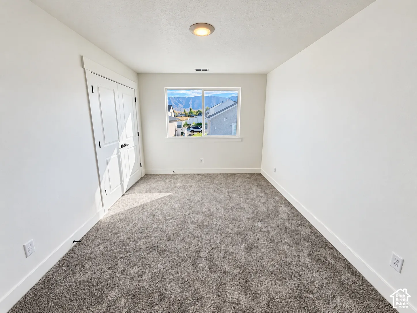 Neutral-toned wall-to-wall carpeting, double-panel closet doors with matte black hardware, and an energy-efficient window with mountain scenery