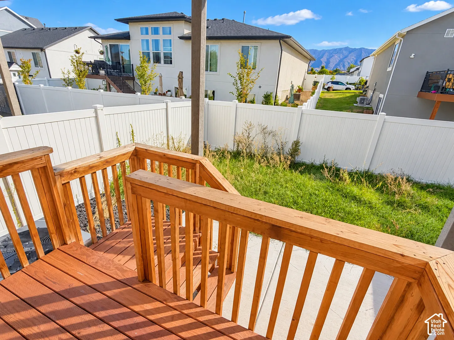Stained wood deck with stair access, white vinyl privacy fencing, concrete patio, and mountain scenery