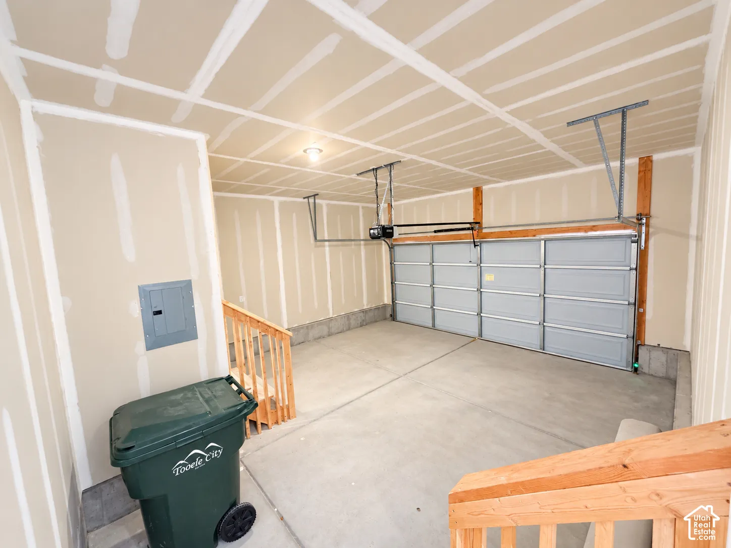 Two-car garage featuring drywall finish, concrete flooring, overhead automatic door opener, and integrated wooden staircase