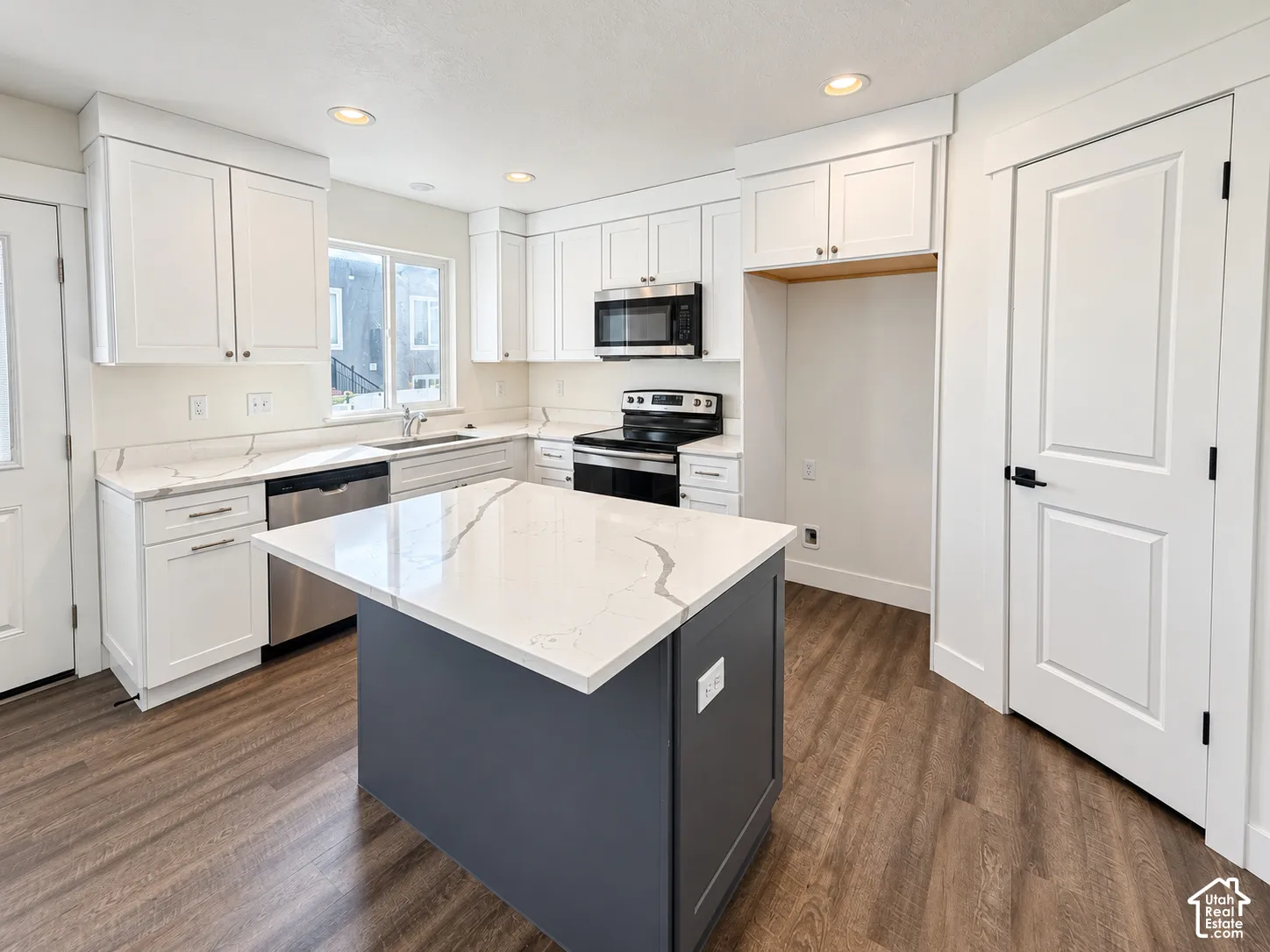 Kitchen featuring white shaker-style cabinetry, quartz countertops with veining, a central island with a contrasting dark base, stainless steel appliances, and wood-finish flooring
