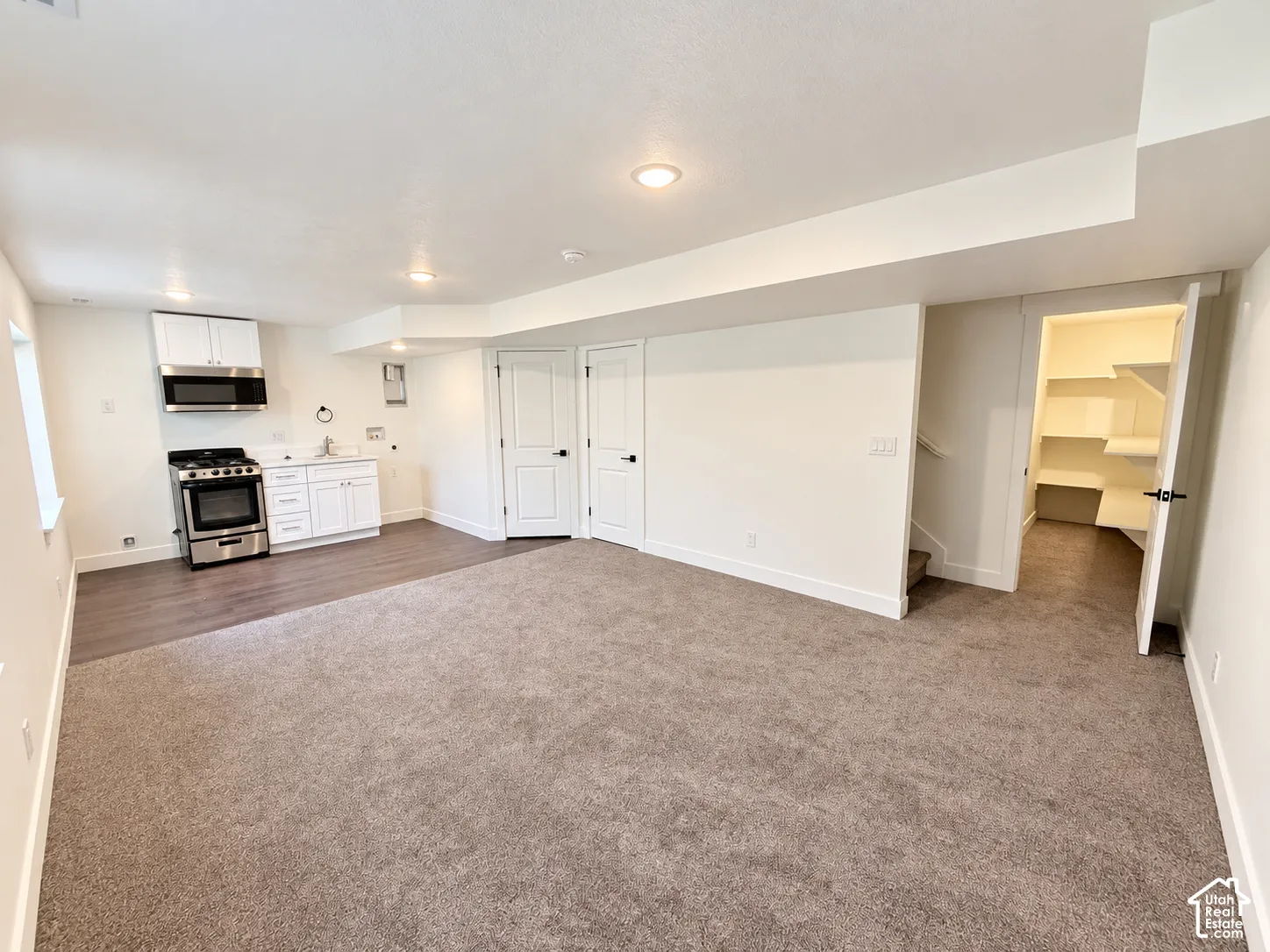 Kitchenette featuring white cabinetry, a stainless steel range, and a built-in microwave, complemented by neutral carpeting, wood-finish flooring, and a walk-in storage area with integrated shelving