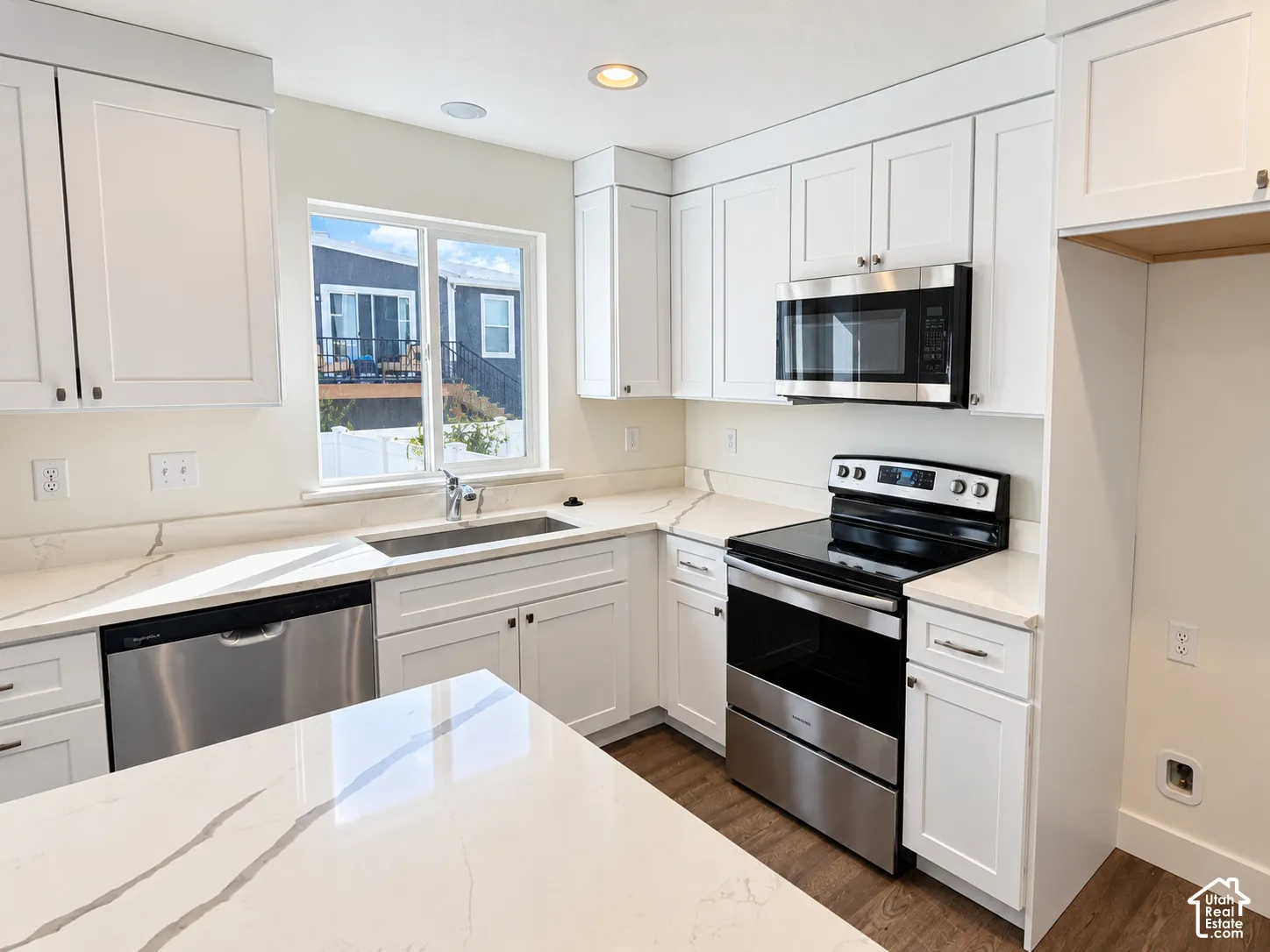 Kitchen featuring white Shaker-style cabinetry, quartz countertops with veining, stainless steel appliances, a stainless steel undermount sink, and wood-finish flooring