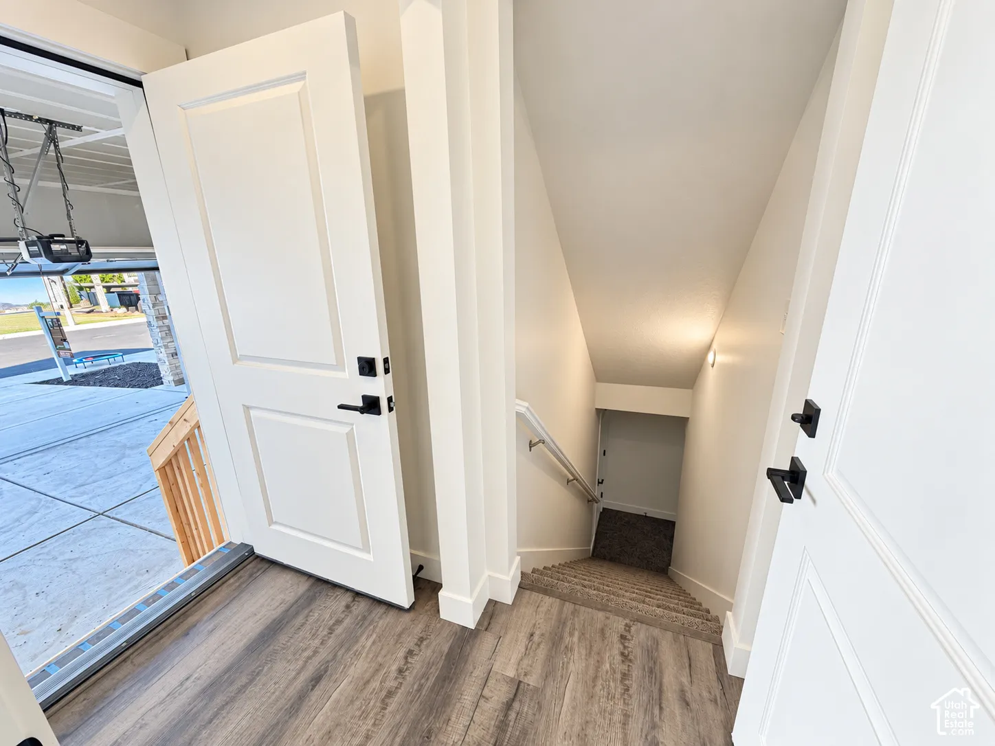 Wood-finish flooring, paneled interior doors with matte black hardware, carpeted staircase with a metal handrail, and white-painted trim