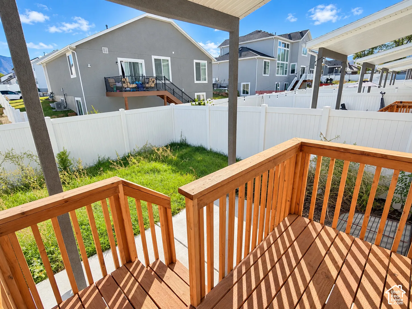 Outdoor deck with wood-finish decking and railings, white vinyl fencing, and concrete patio