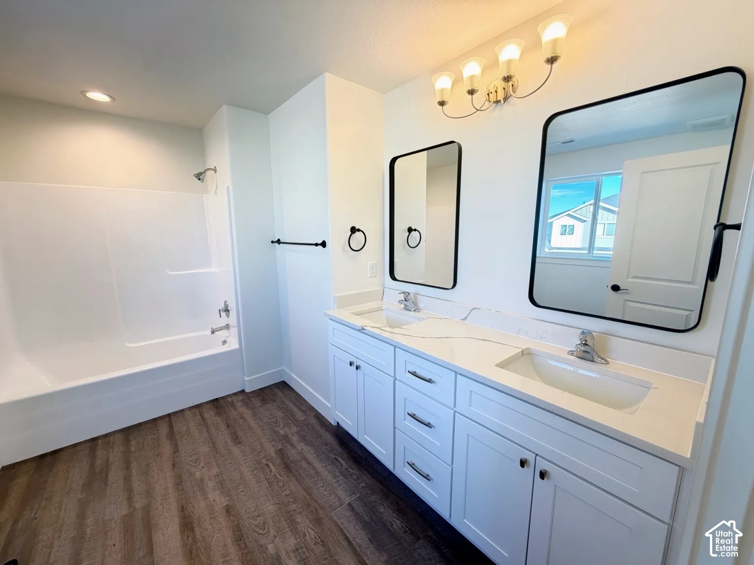 Dual-sink vanity with white cabinetry and stone-composite countertop, matching rectangular mirrors with black frames, and wood-finish flooring