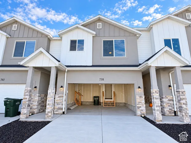 Multi-level exterior featuring vertical siding, stone masonry pillars, integrated concrete garage flooring, and gable rooflines