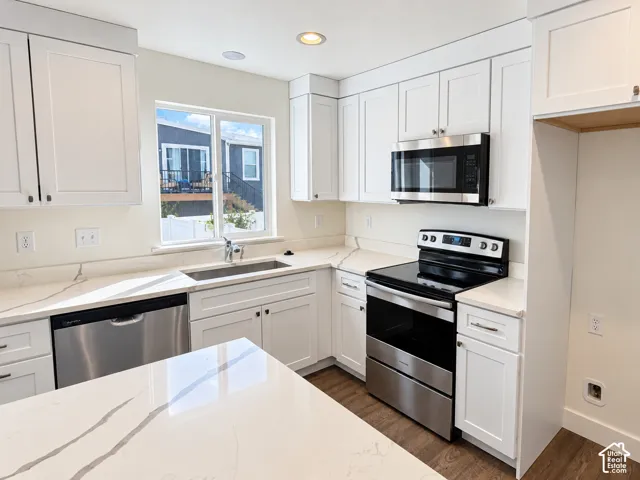 Kitchen featuring white Shaker-style cabinetry, quartz countertops with veining, stainless steel appliances, a stainless steel undermount sink, and wood-finish flooring