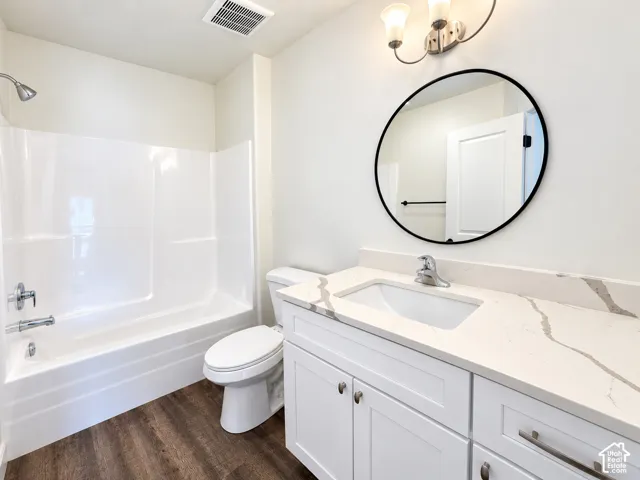 Bathroom featuring a vanity with stone-patterned countertop, undermount sink, round wall mirror with black frame, shower-tub combination, and wood-finish flooring