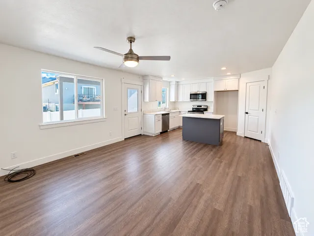 Kitchen featuring white shaker-style cabinetry, dark-toned center island, stainless steel appliances, and wood-finish flooring throughout
