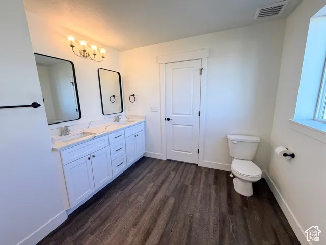 Double-sink vanity with white cabinetry, integrated sinks, and quartz countertop, complemented by dark-finish hardware, two rectangular mirrors, and wood-finish flooring