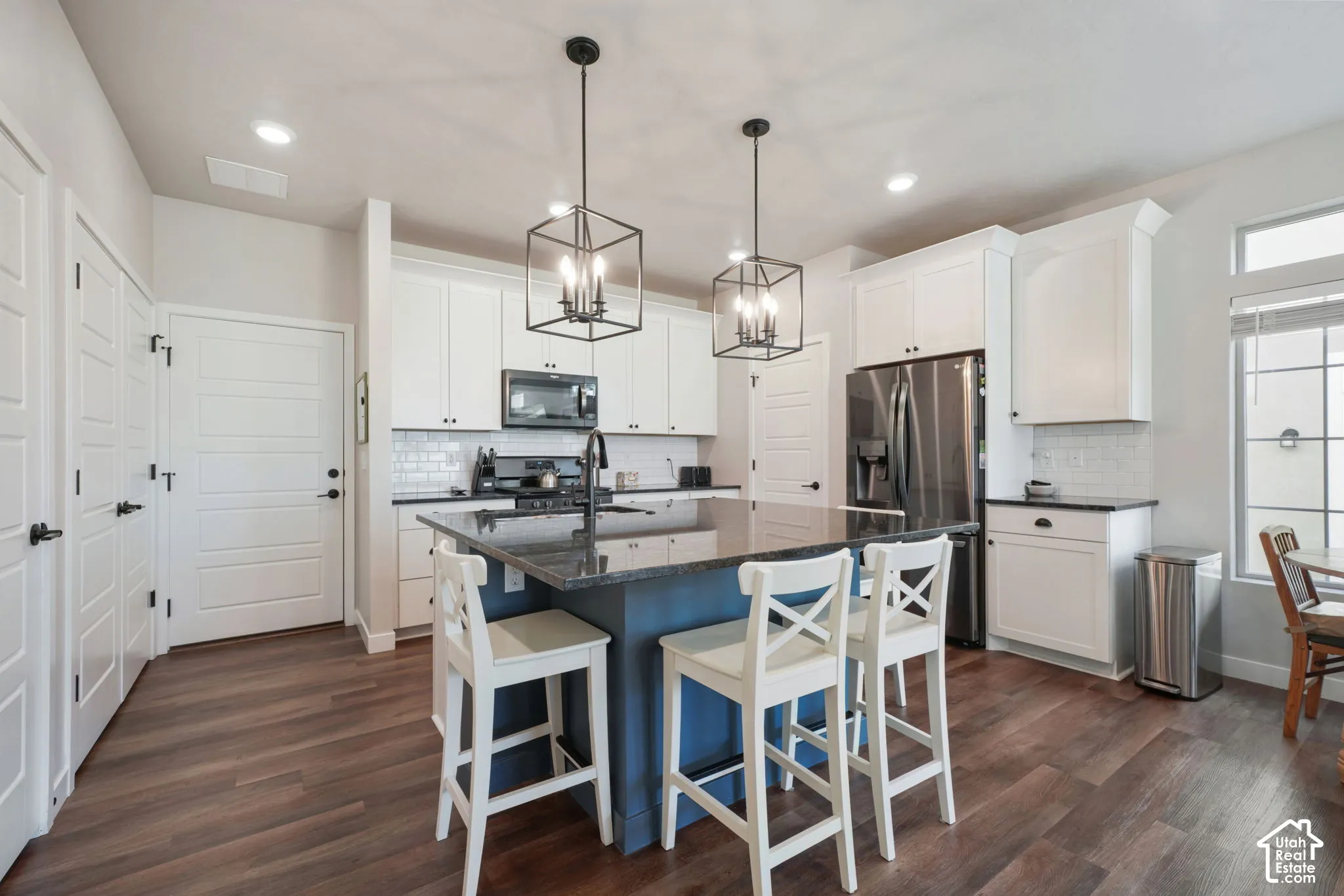 Kitchen featuring white cabinetry, a contrasting blue center island with stone countertop, stainless steel appliances, and wood-finish flooring