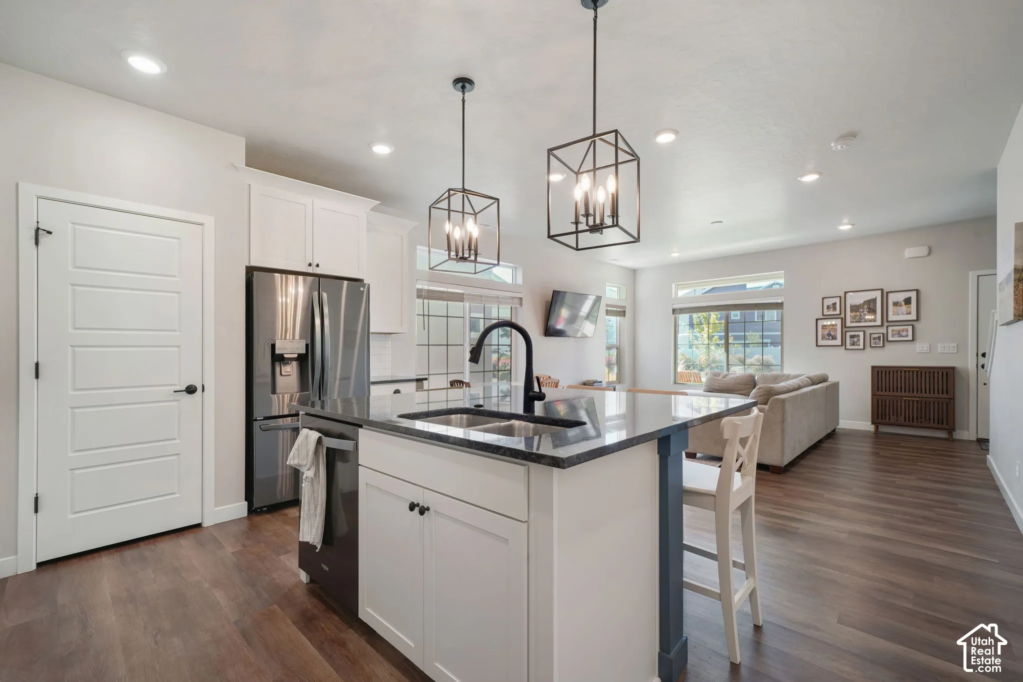 Kitchen island with dual-basin sink and matte black faucet, dark stone-finish countertops, shaker-style cabinetry, wood-finish flooring, and industrial-style geometric pendant lighting