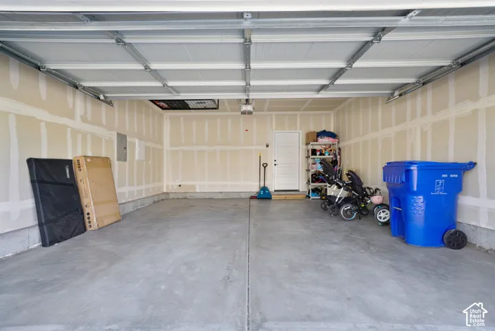 Two-car garage featuring a concrete floor, a sectional overhead door, a dedicated pedestrian side door, and an integrated ceiling-mounted automatic garage door opener