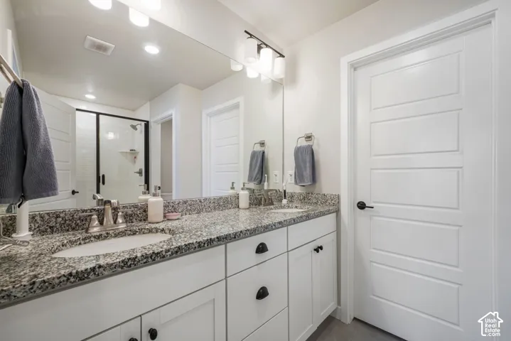 Dual-sink vanity with stone-finish countertop, white shaker-style cabinetry, matte black hardware, full-width mirror, and a shower enclosure with a dark-finish frame