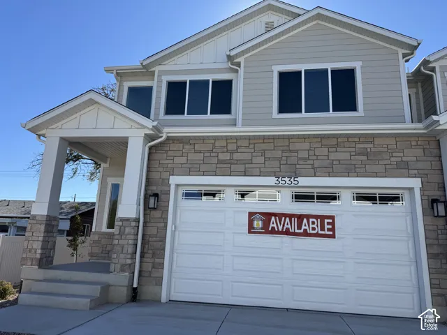 Exterior featuring multi-textured facade with stone veneer and horizontal siding, covered entryway with stone-clad columns, and a two-car garage with transom window accents