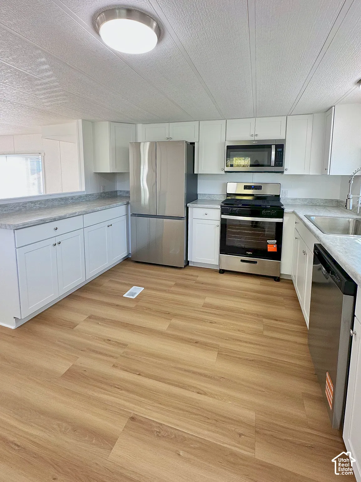Kitchen featuring white shaker-style cabinetry, neutral-toned countertops, wood-finish flooring, and stainless steel appliances including a refrigerator, gas range, microwave, and dishwasher