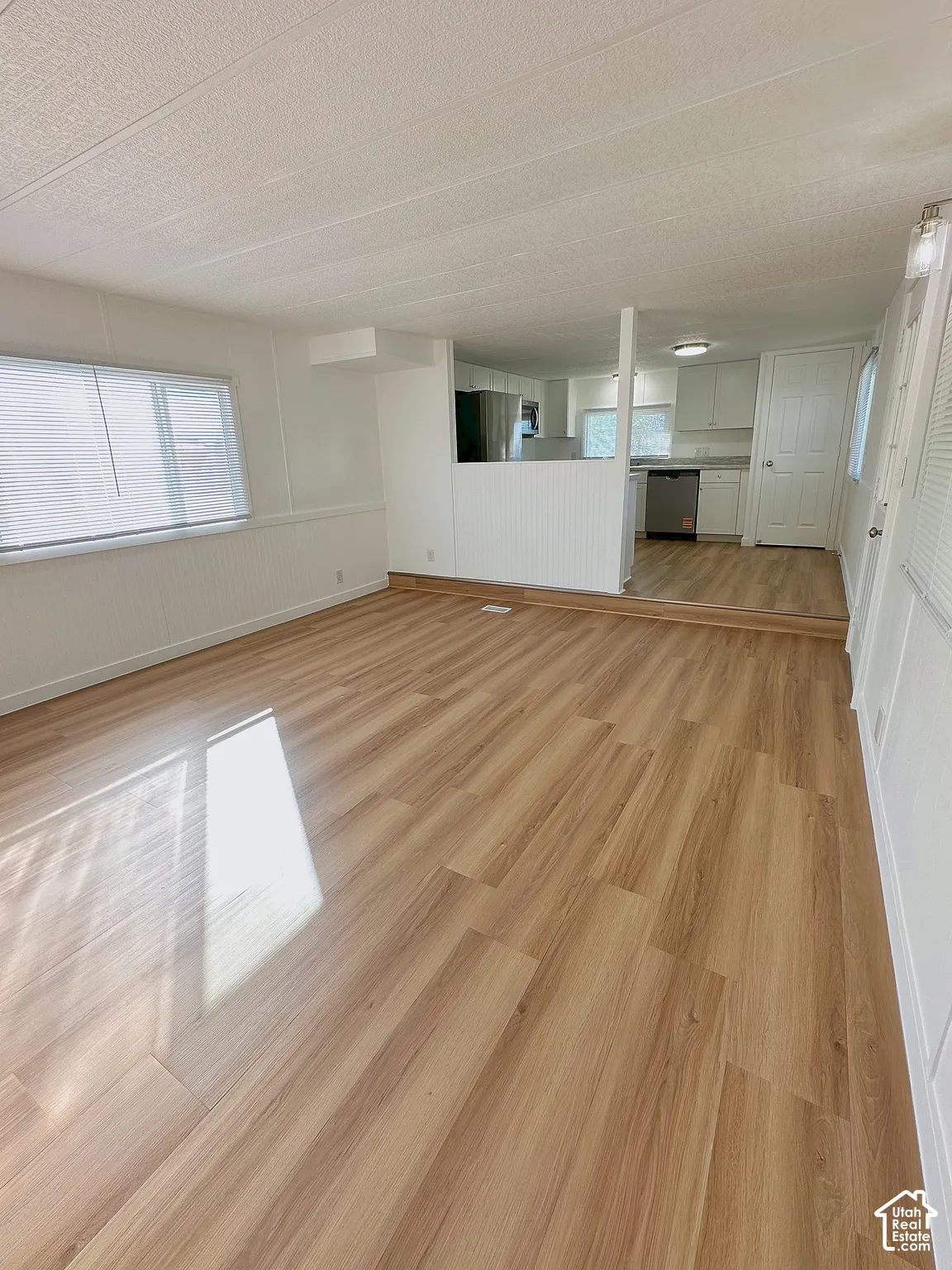 Open-concept interior featuring light-tone wood-finish flooring, white beadboard wall paneling, and a tiered floor elevation