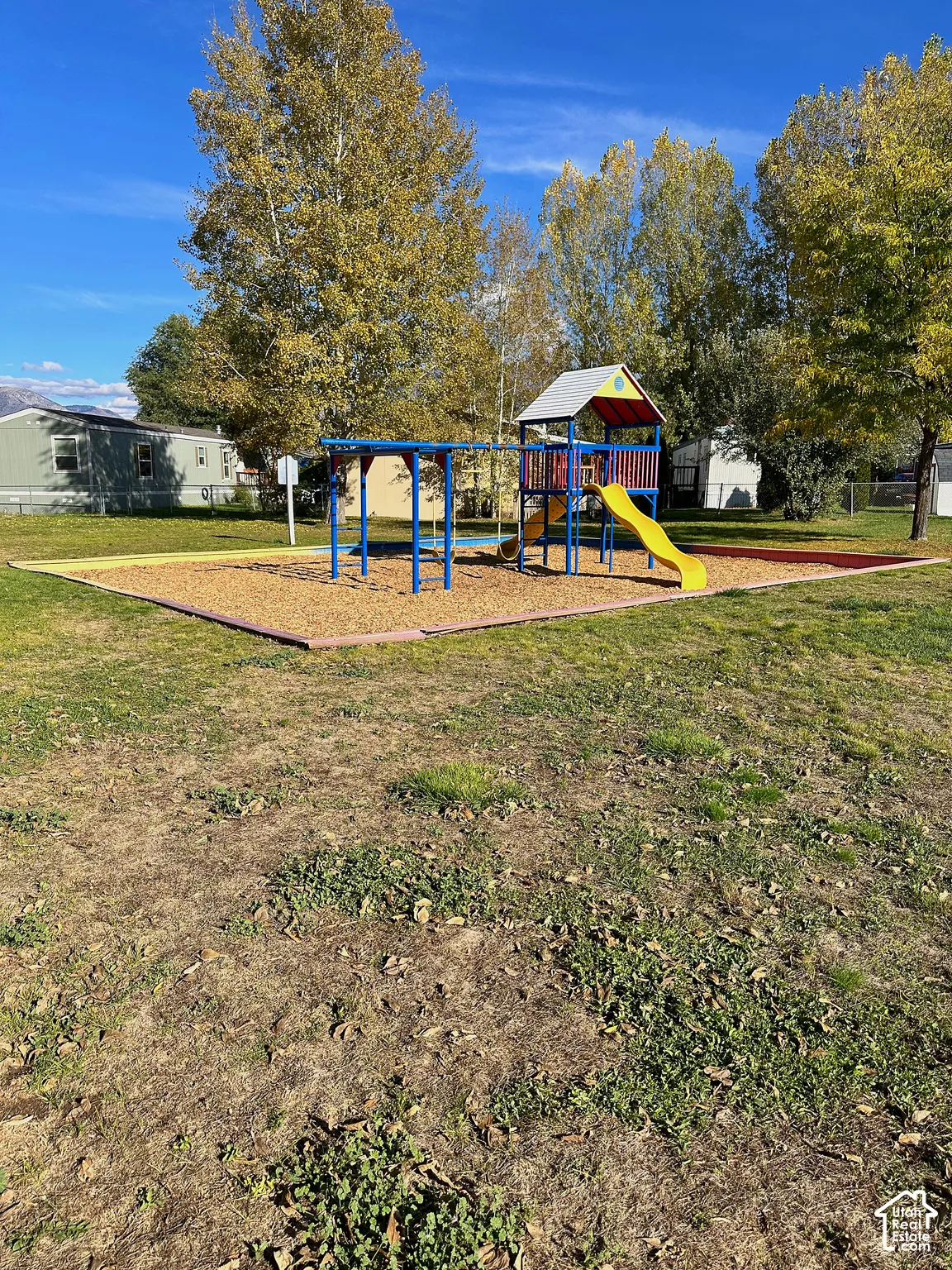 Outdoor recreation area featuring a metal play structure, wood chip ground cover, and defined perimeter curbing