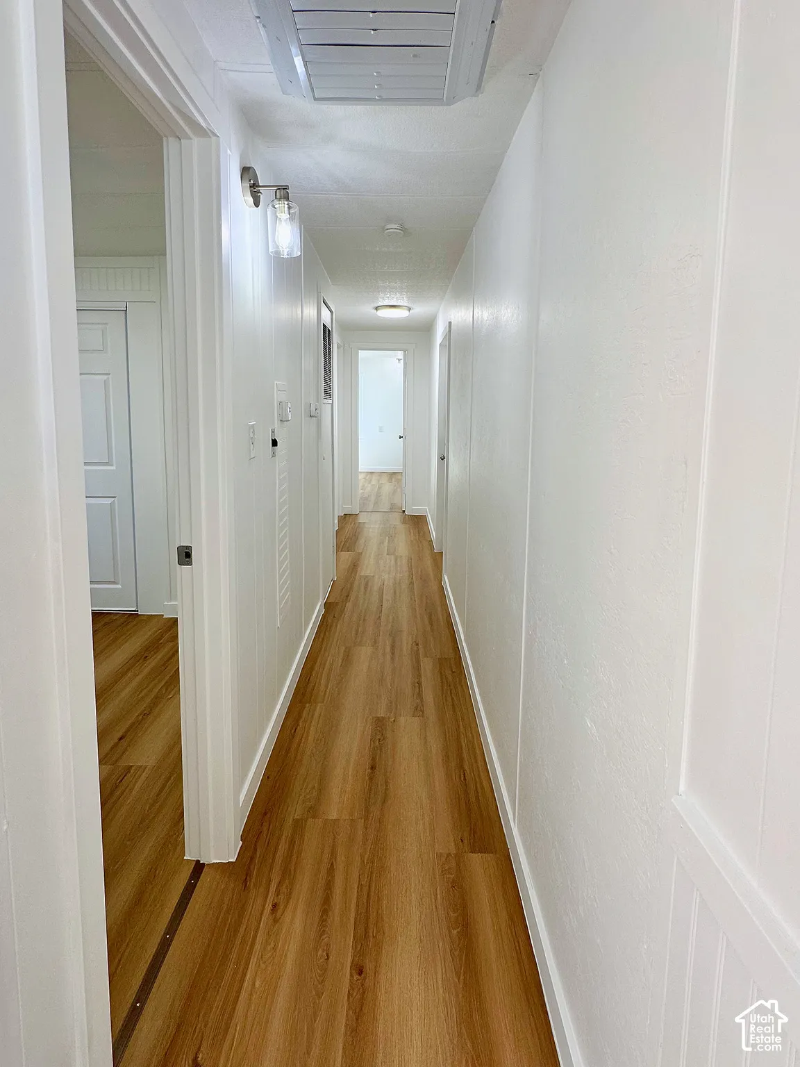 Hallway featuring wood-finish flooring, white paneled wall accents, and wall-mounted light fixtures