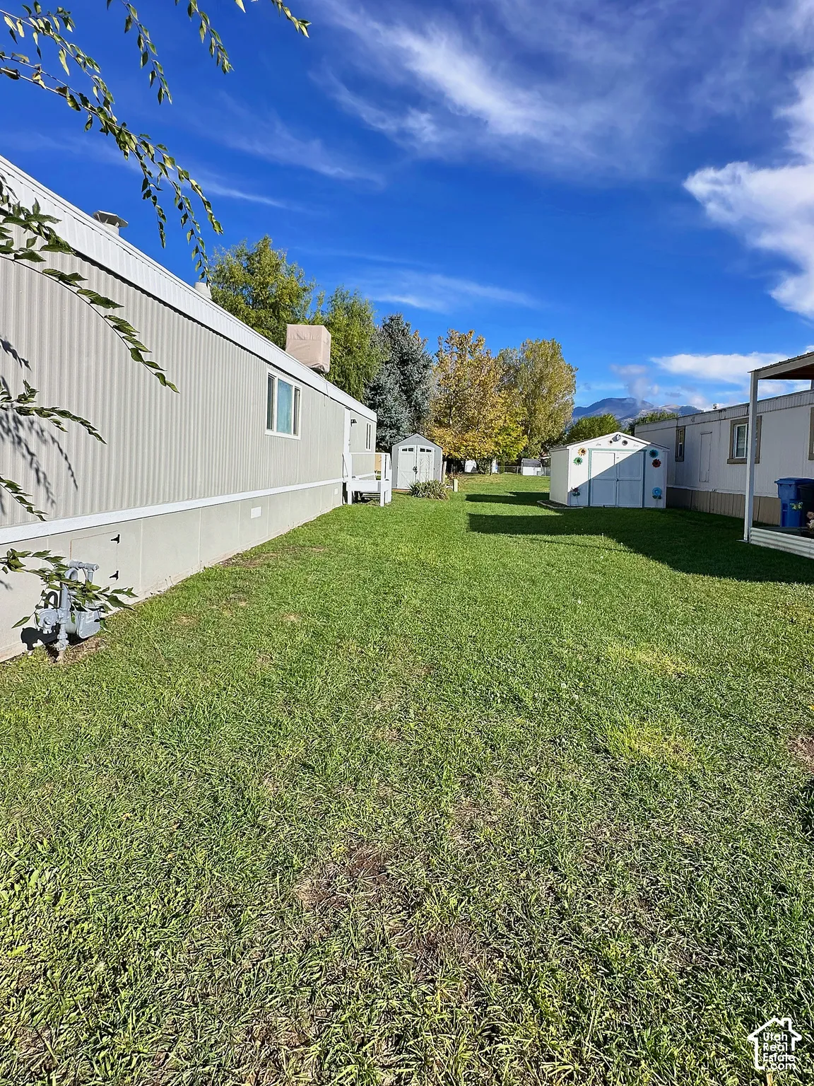 Expansive side yard featuring a grass lawn, two detached storage structures, and mountain scenery