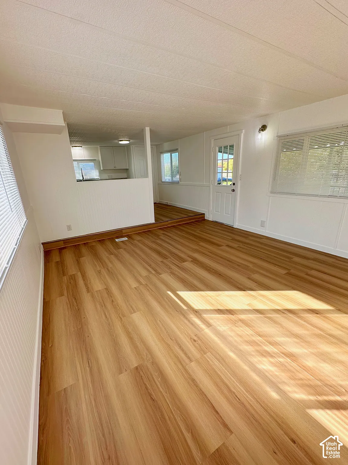 Interior space featuring wood-finish flooring, white beadboard wainscoting, a textured ceiling, and a glass-paneled entry door