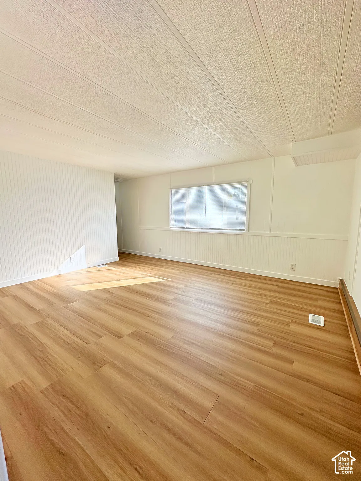 Neutral-toned living space featuring wood-finish flooring, white beadboard-style wall paneling, and a horizontal window with installed blinds