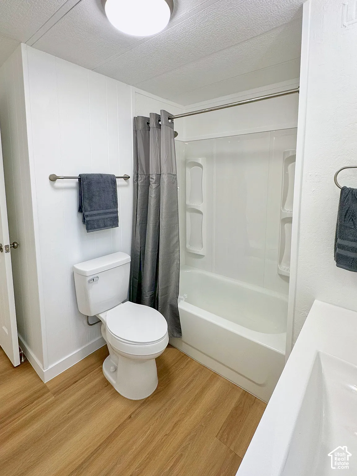 Full bathroom featuring a tub-shower combination with built-in shelving, wood-finish flooring, and a round-front toilet