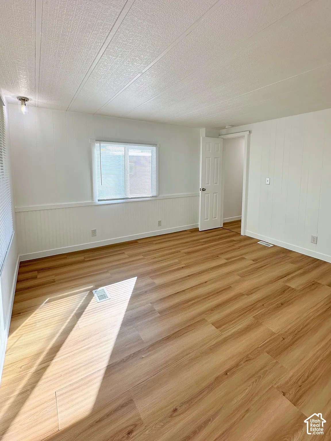 Interior room featuring wood-finish flooring, white paneling with chair rail molding, and a single-pane sliding window