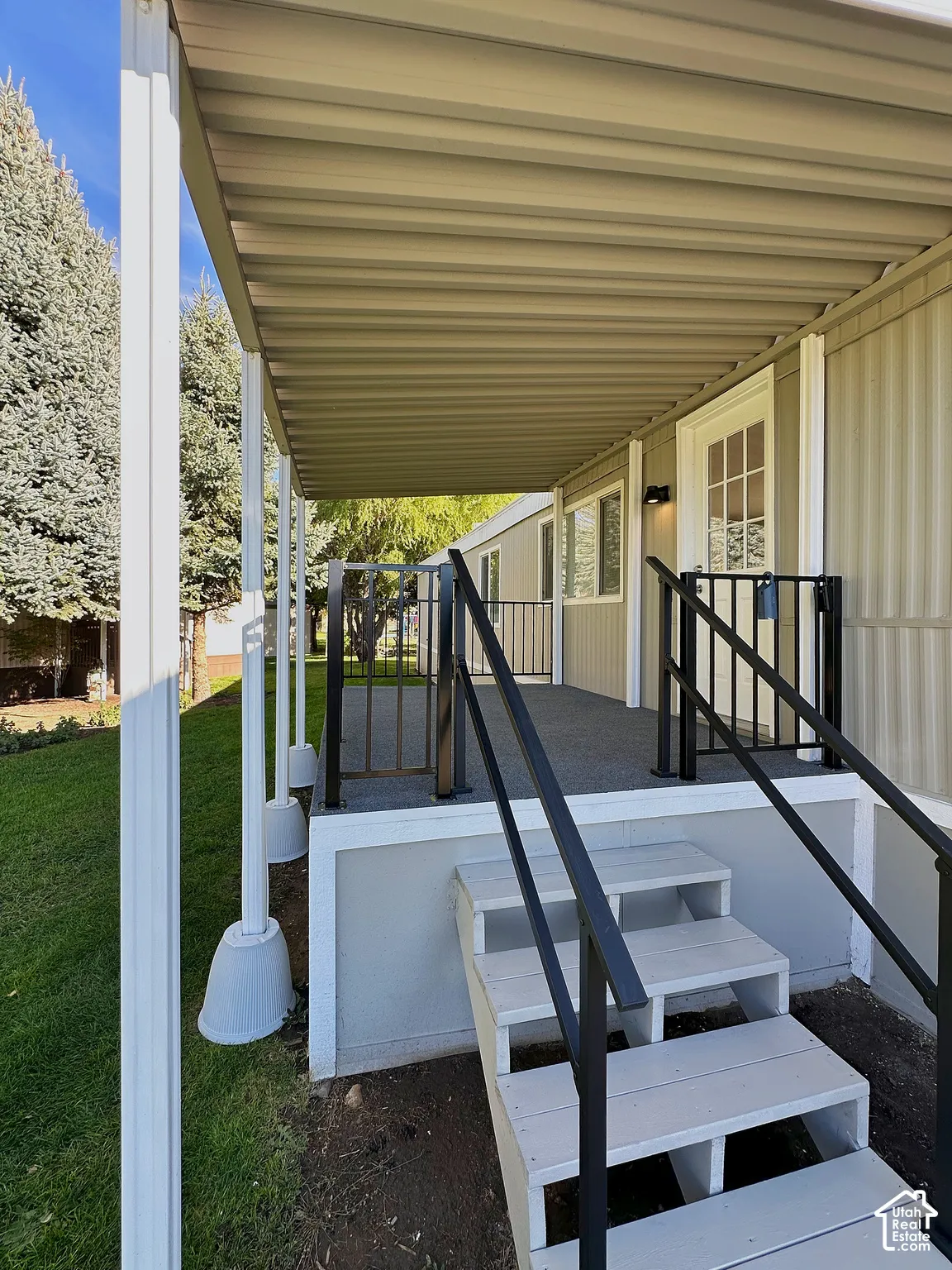 Covered exterior porch featuring a textured surface, white vertical support pillars, and black metal railings with matching stair handrails