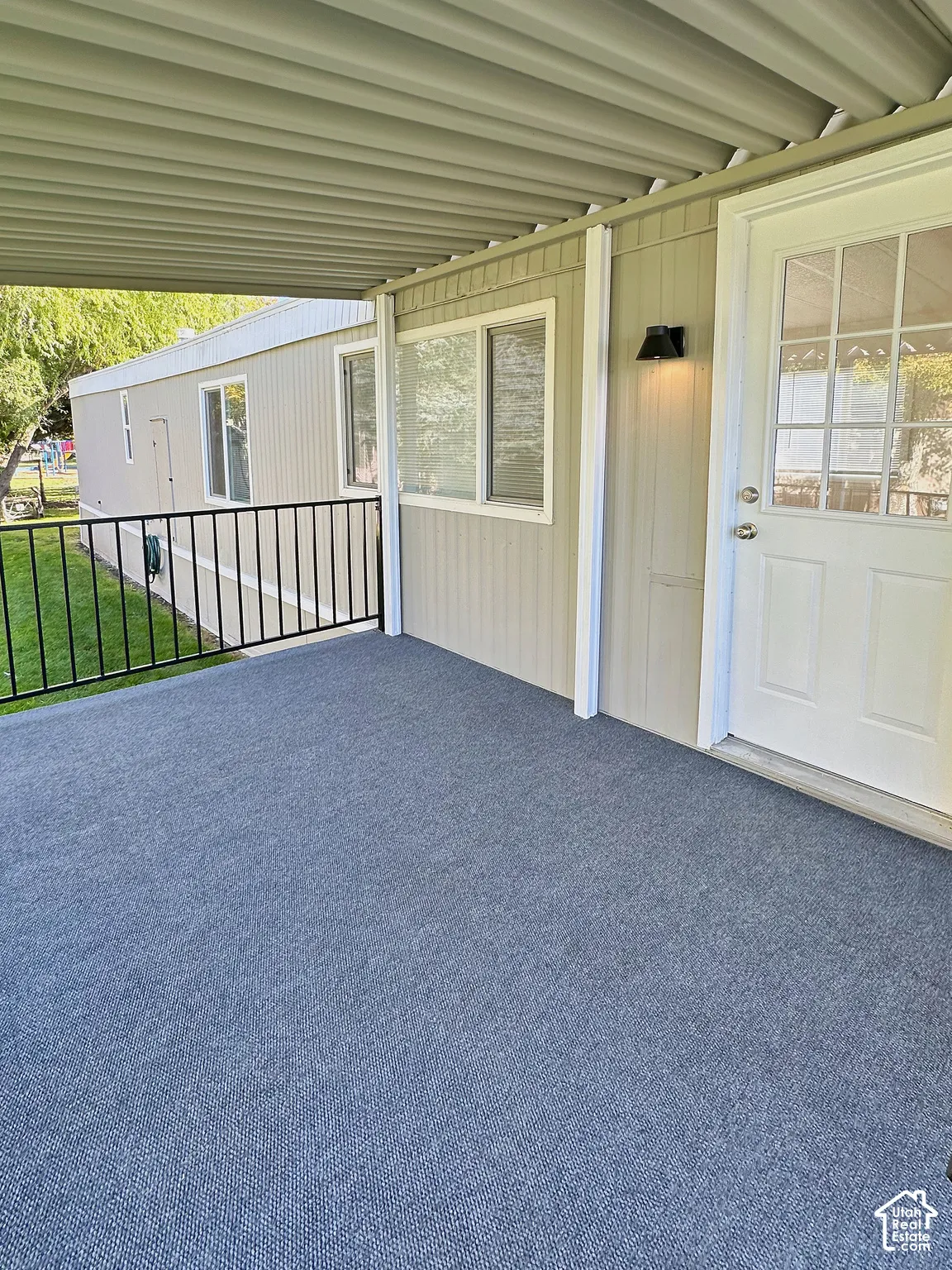 Covered porch featuring a corrugated metal roof, gray outdoor carpeting, and black metal railing