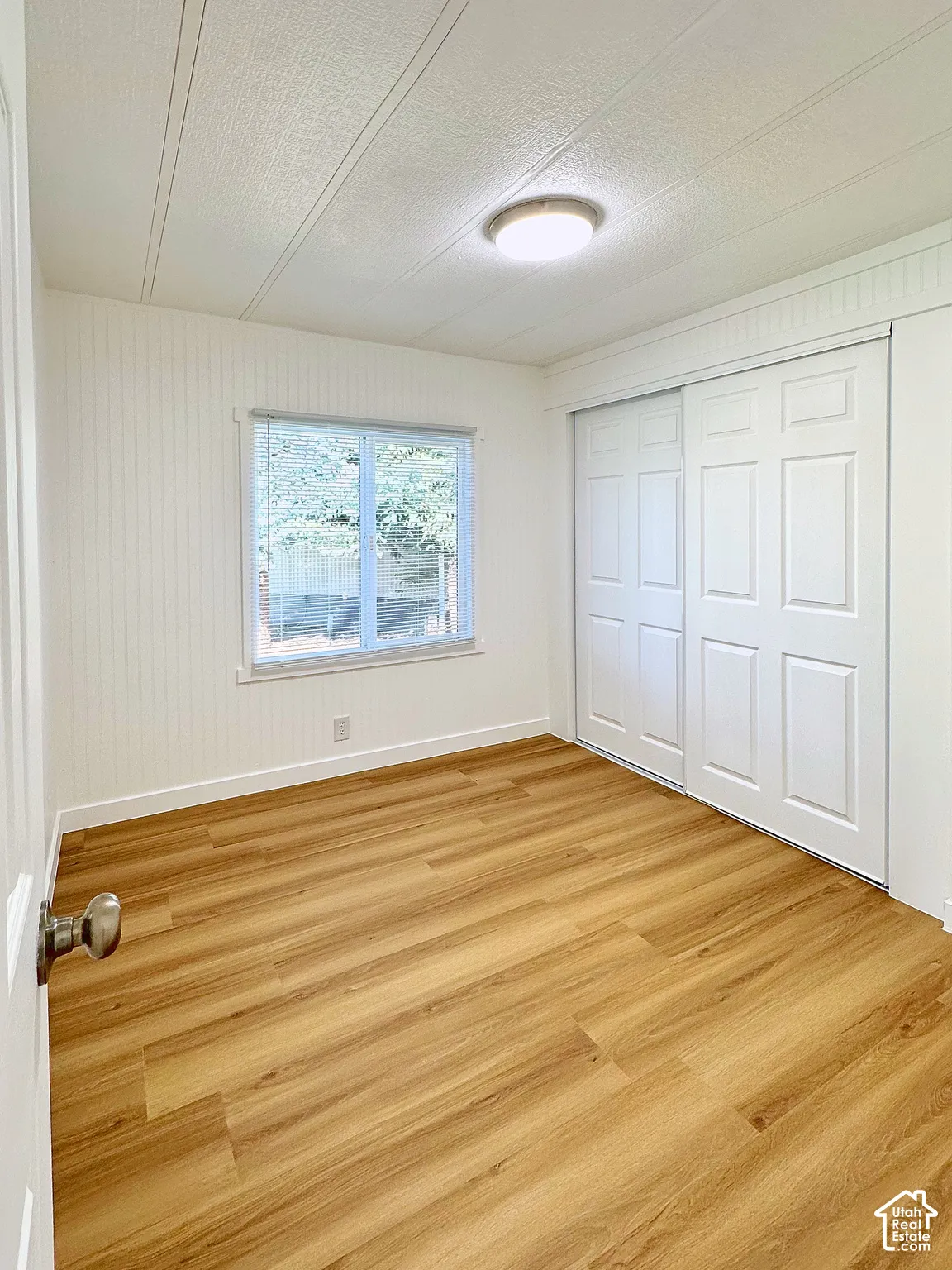 Room featuring wood-finish flooring, vertical paneling, a sliding-door closet, and a single-pane window with mini-blinds