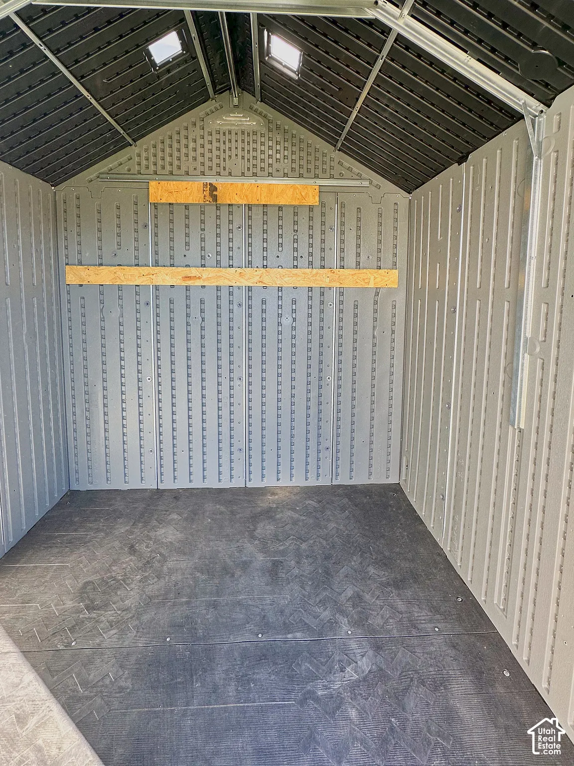 Detached storage structure featuring high-density resin paneled walls, a reinforced dark-tone flooring, integrated overhead skylights, and horizontal wood-finish wall-mounted shelving