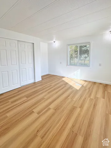 Wood-finish flooring, white paneling, sliding-door closet, and window with built-in blinds