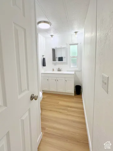 Bathroom featuring wood-finish flooring, white cabinetry with integrated countertop, recessed ceiling lighting, and a medicine cabinet with mirror