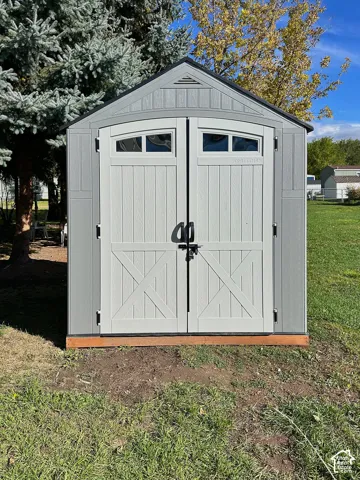 Exterior storage shed featuring a gabled roof, double doors with glass insets, and a wood foundation frame