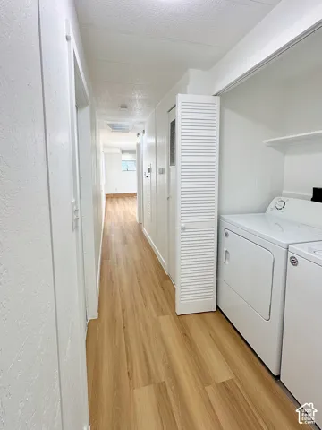 Hallway featuring wood-finish flooring, white louvered closet doors, and overhead shelving