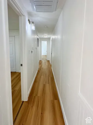 Hallway featuring wood-finish flooring, white paneled wall accents, and wall-mounted light fixtures