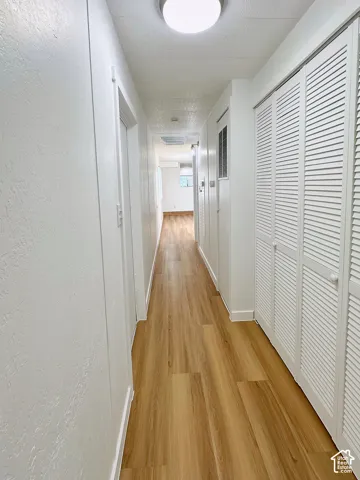 Hallway featuring wood-finish flooring, ceiling-mounted lighting, and built-in white louvered closet doors