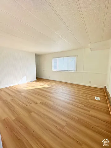 Neutral-toned living space featuring wood-finish flooring, white beadboard-style wall paneling, and a horizontal window with installed blinds