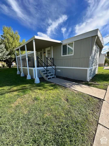 Exterior featuring vertical metal siding, a covered porch with metal railing, and a concrete walkway