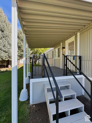 Covered exterior porch featuring a textured surface, white vertical support pillars, and black metal railings with matching stair handrails