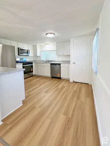 Kitchen featuring white shaker-style cabinetry, wood-finish flooring, stone-patterned countertops, and stainless steel appliances