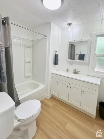 Bathroom featuring a white vanity cabinet with a solid surface countertop, an integrated sink, a multi-panel medicine cabinet, a tub-shower combination with built-in shelving, and wood-finish flooring
