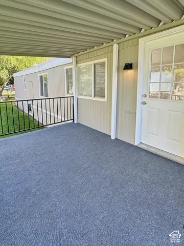 Covered porch featuring a corrugated metal roof, gray outdoor carpeting, and black metal railing