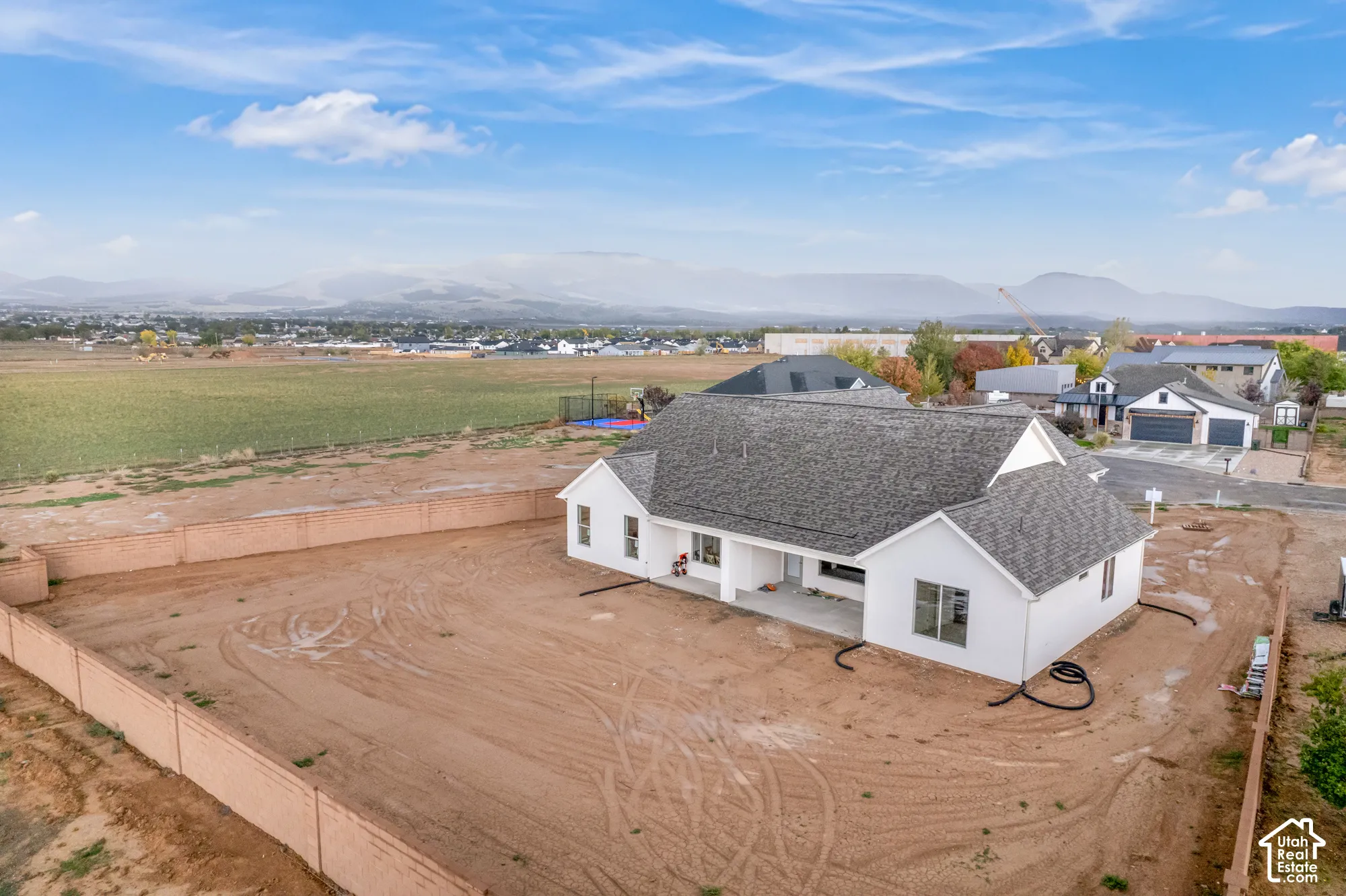 Single-story residence featuring a neutral exterior, multi-pitched shingle roof, expansive fenced perimeter, and a mountainous backdrop